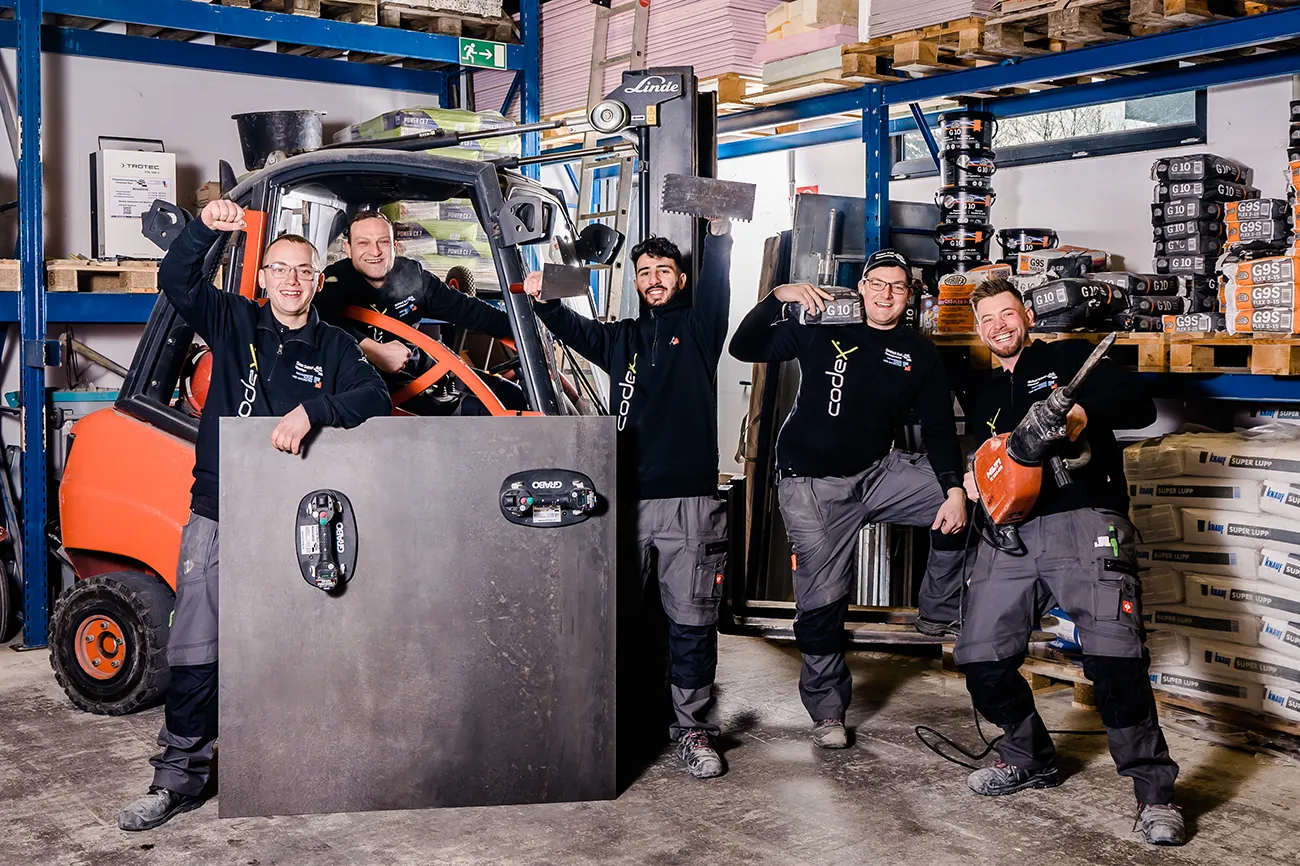 Das gesamte Team von Fliesenleger Kast aus Heimbach posiert gemeinsam im Lager mit Baustoffen und Werkzeug